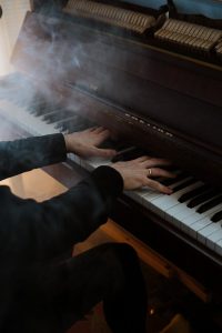 Hands gracefully play a grand piano surrounded by a mysterious smoky atmosphere.